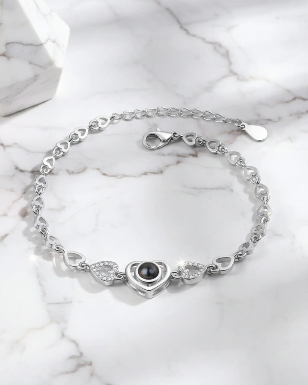 Armbånd med hjerteformede led og en hjertecharm, hvor en lille sten skjuler et billede indeni.