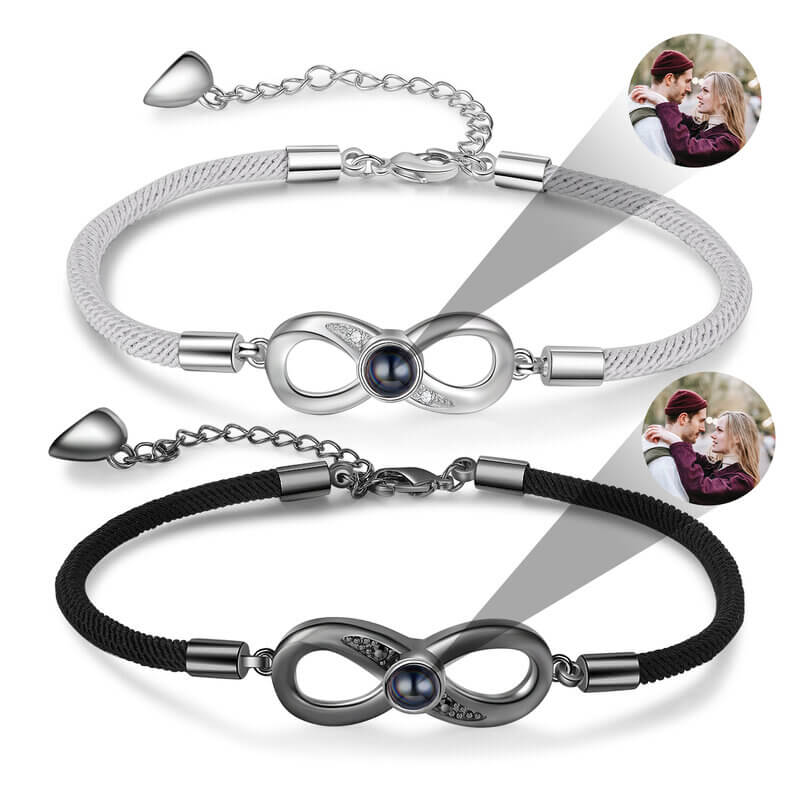 To armbånd i hvid og sort kobber med et uendelighedsvedhæng, der gemmer et billede bag en linse.
