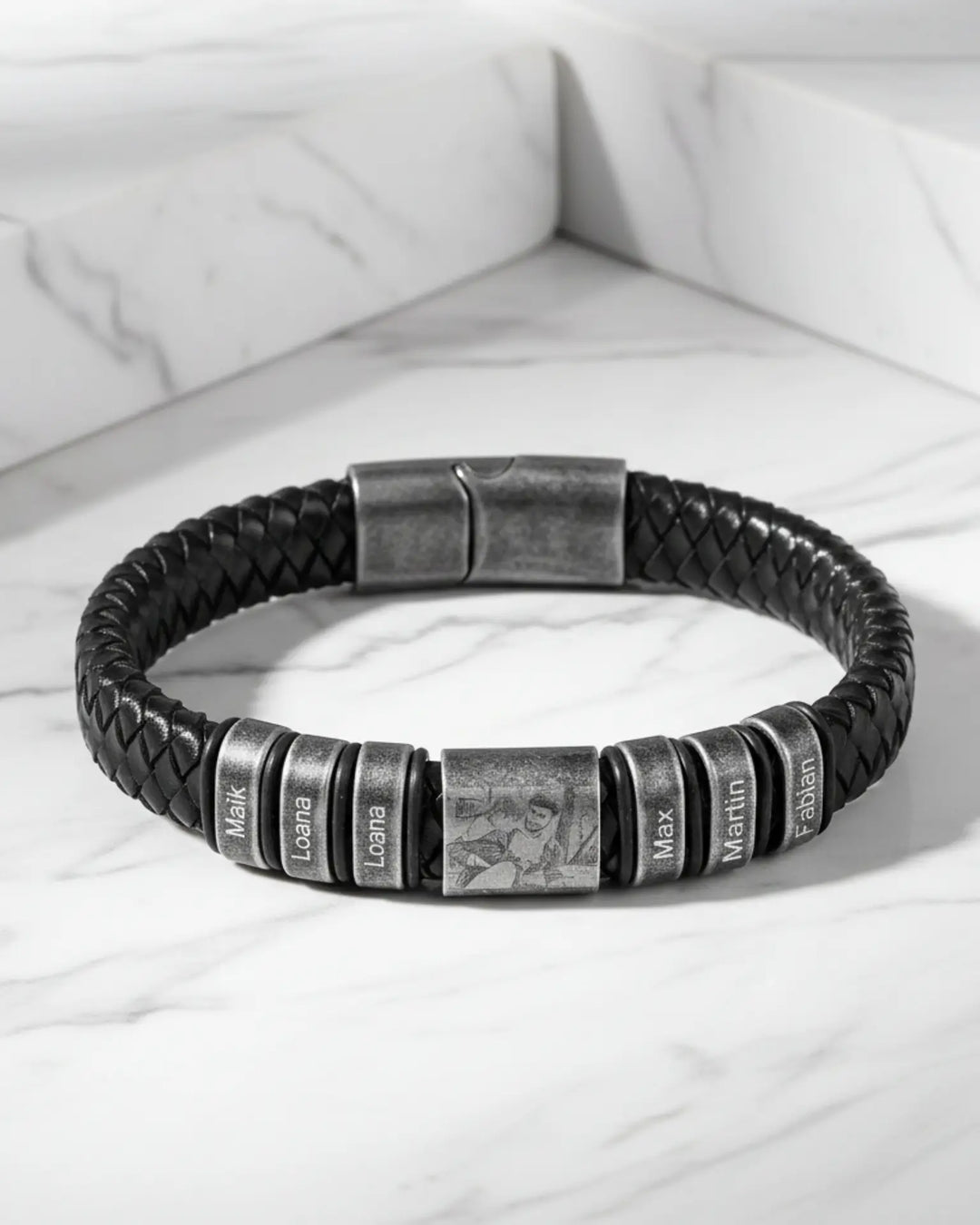 Bredt flettet læderarmbånd til mænd med en plade med indgraveret billede og flere små navnecharms i stål.