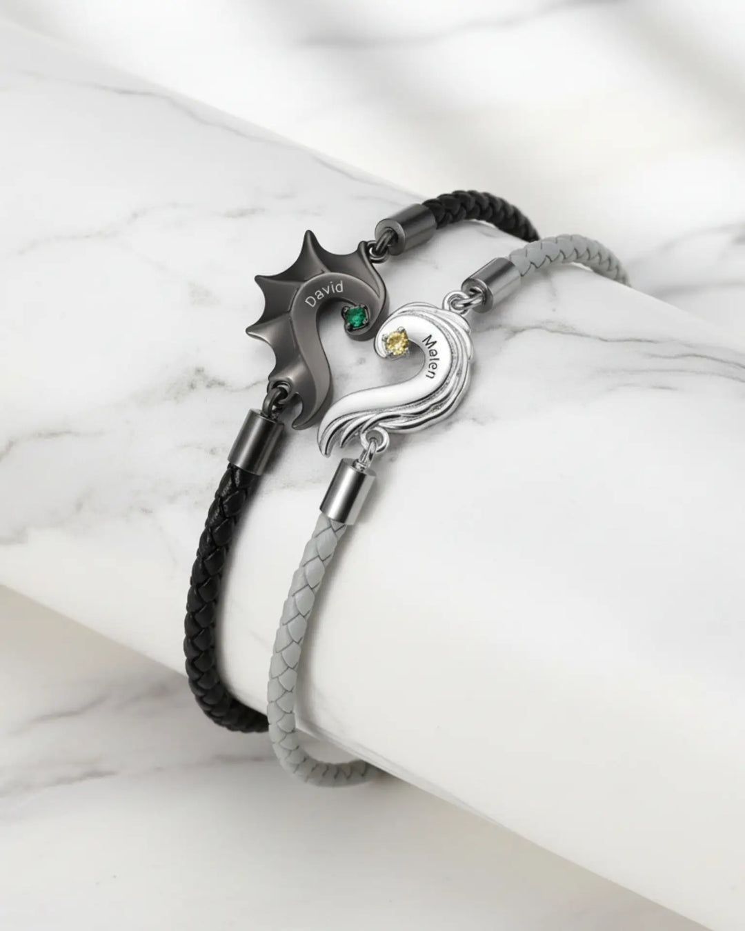 To læderarmbånd i sort og lyst med hver sin halvdel af et hjerte formet som drage- og englevinge.