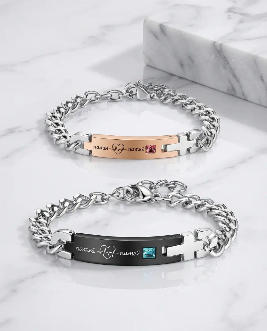 To matchende armbånd i rustfrit stål med en plade, hvor en hjerteslagslinje og et navn er indgraveret.
