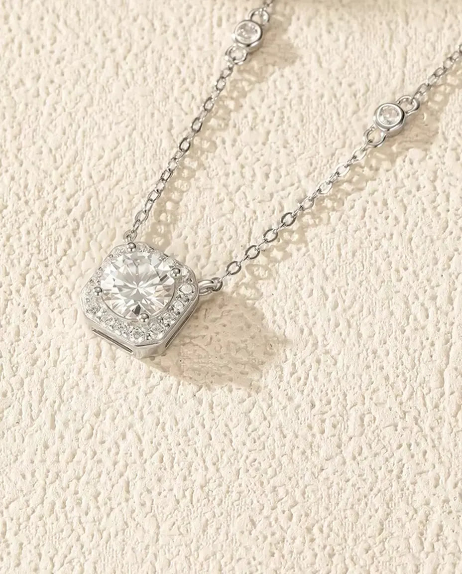Rund moissanite i en pudeformet halo på en kæde med fire små indfattede sten i 925 sterling sølv.