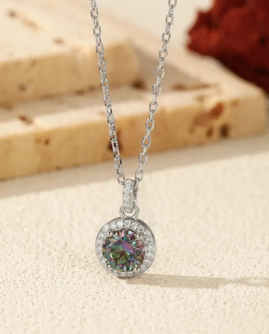 Rund moissanite i turkisblå tone omkranset af klare pavésten i rhodineret 925 sterling sølv.