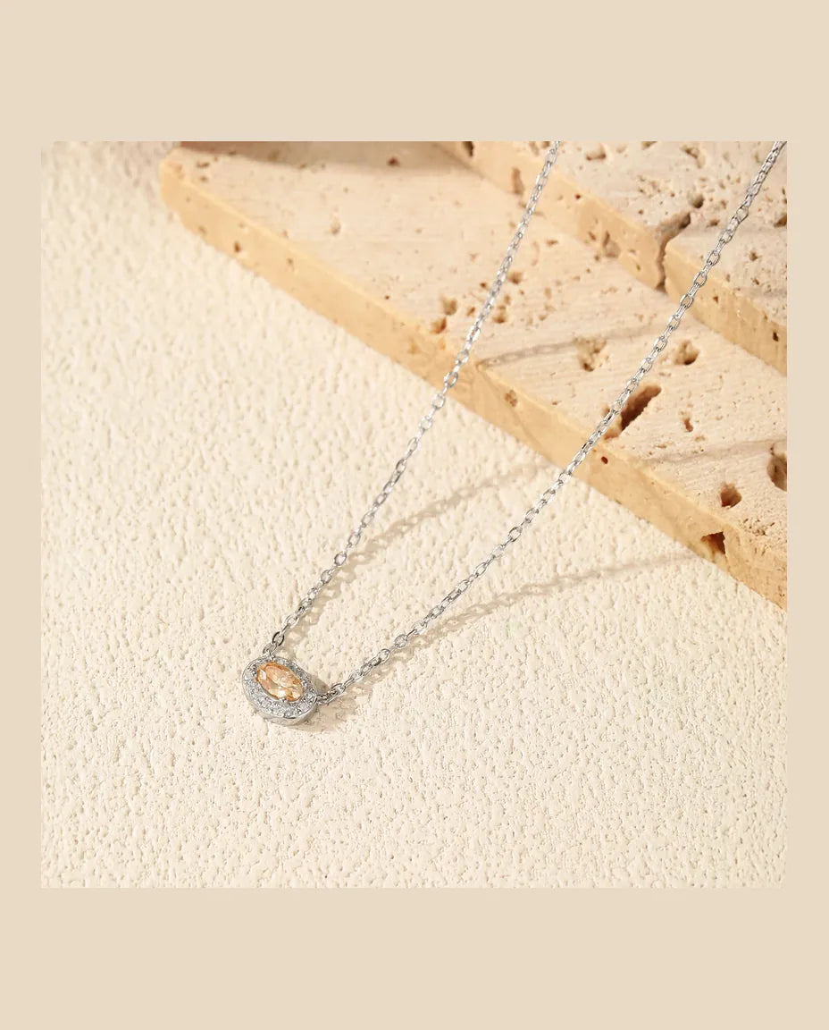 Gul oval moissanite lagt på tværs i en halo af hvide sten i rhodineret 925 sterling sølv.