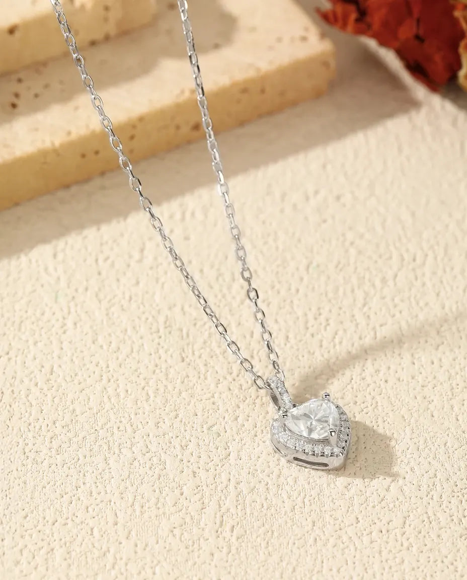 Hjerteformet moissanite omkranset af en halo af små klare sten i rhodineret 925 sterling sølv.
