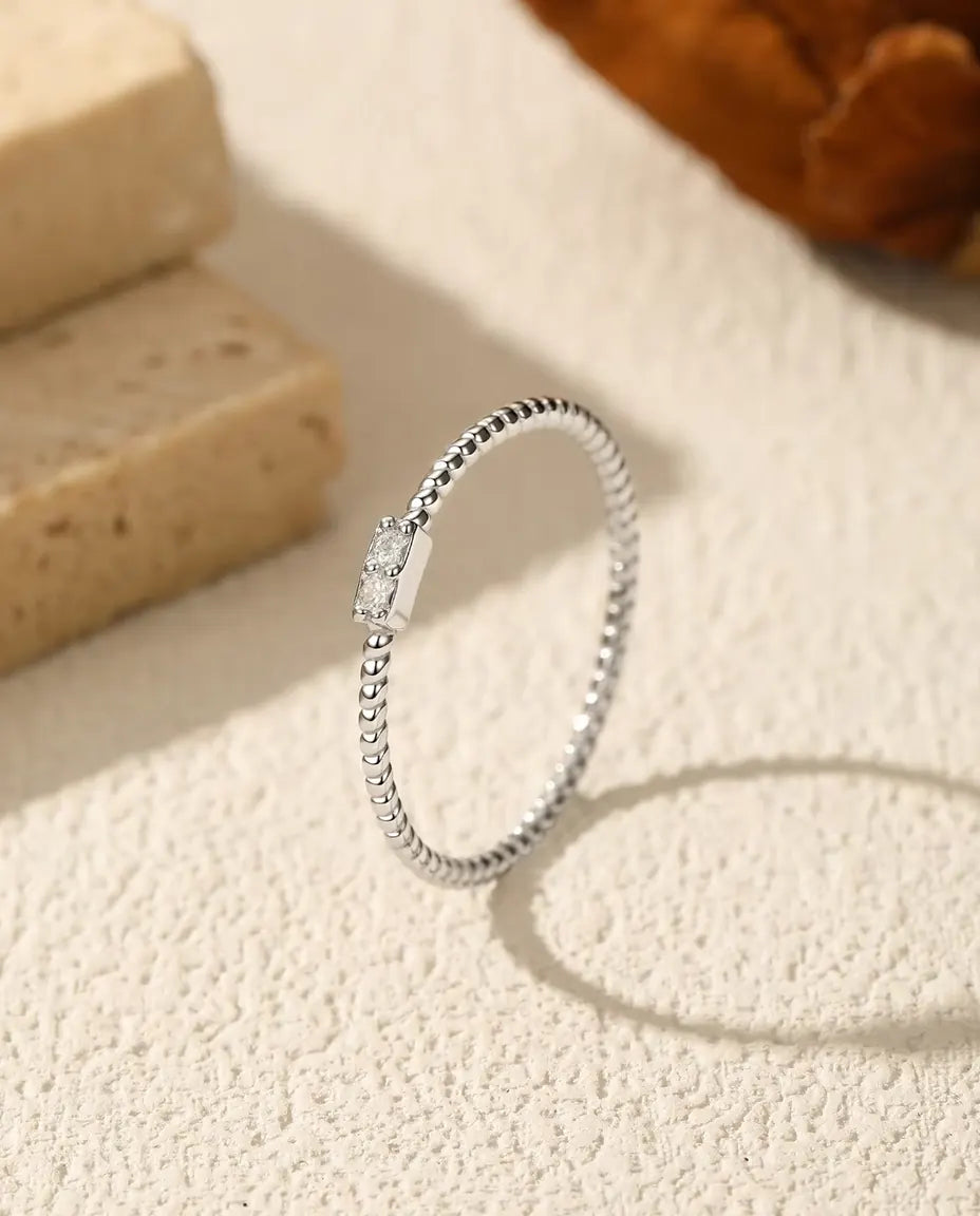 Smal sølvring med snoet skinne og to små moissanite på en poleret plade i 925 sterling sølv.