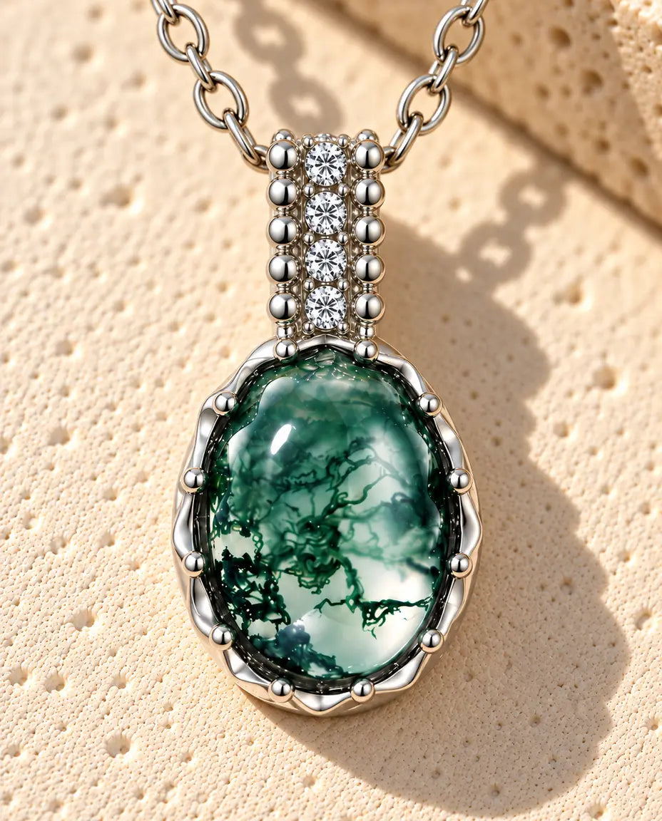 Sølvhalskæde med en grøn oval moss agate-cabochon i en bølget kant under en søjleformet øsken på beige puds foran travertin.