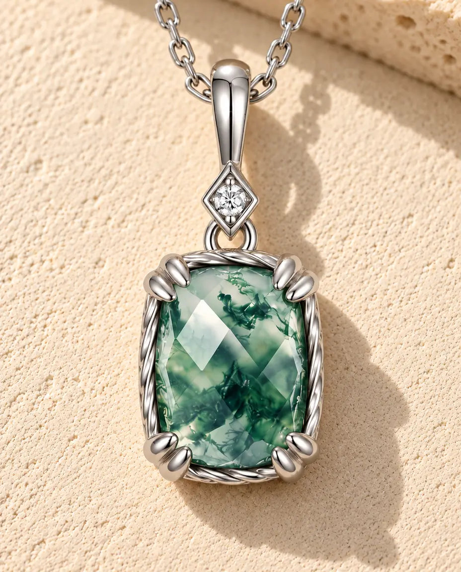 Sølvhalskæde med en grøn skakbrætslebet moss agate i snoet ramme under et led med zirkonia på beige puds foran travertin.