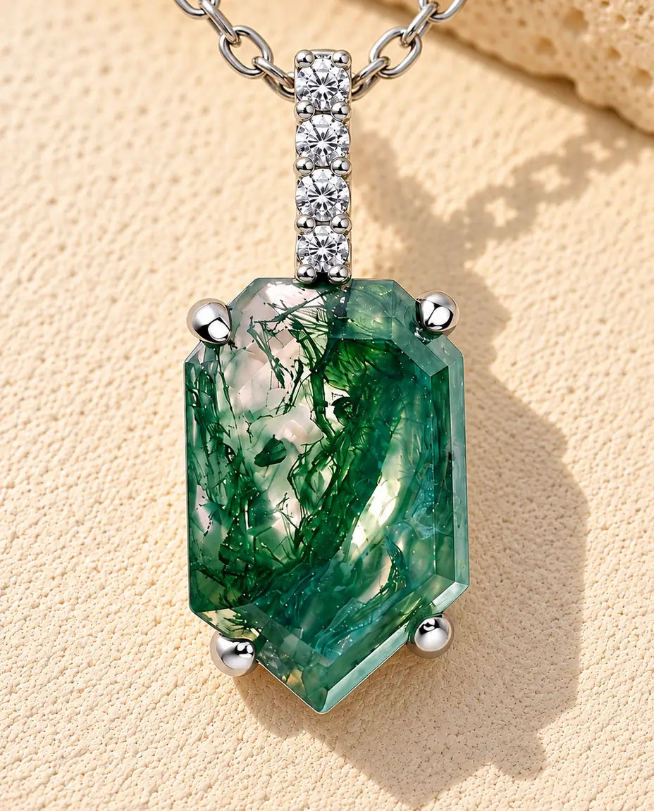 Sølvhalskæde med en skjoldformet, facetteret grøn moss agate under en smal øsken med fire hvide zirkonia på beige puds.