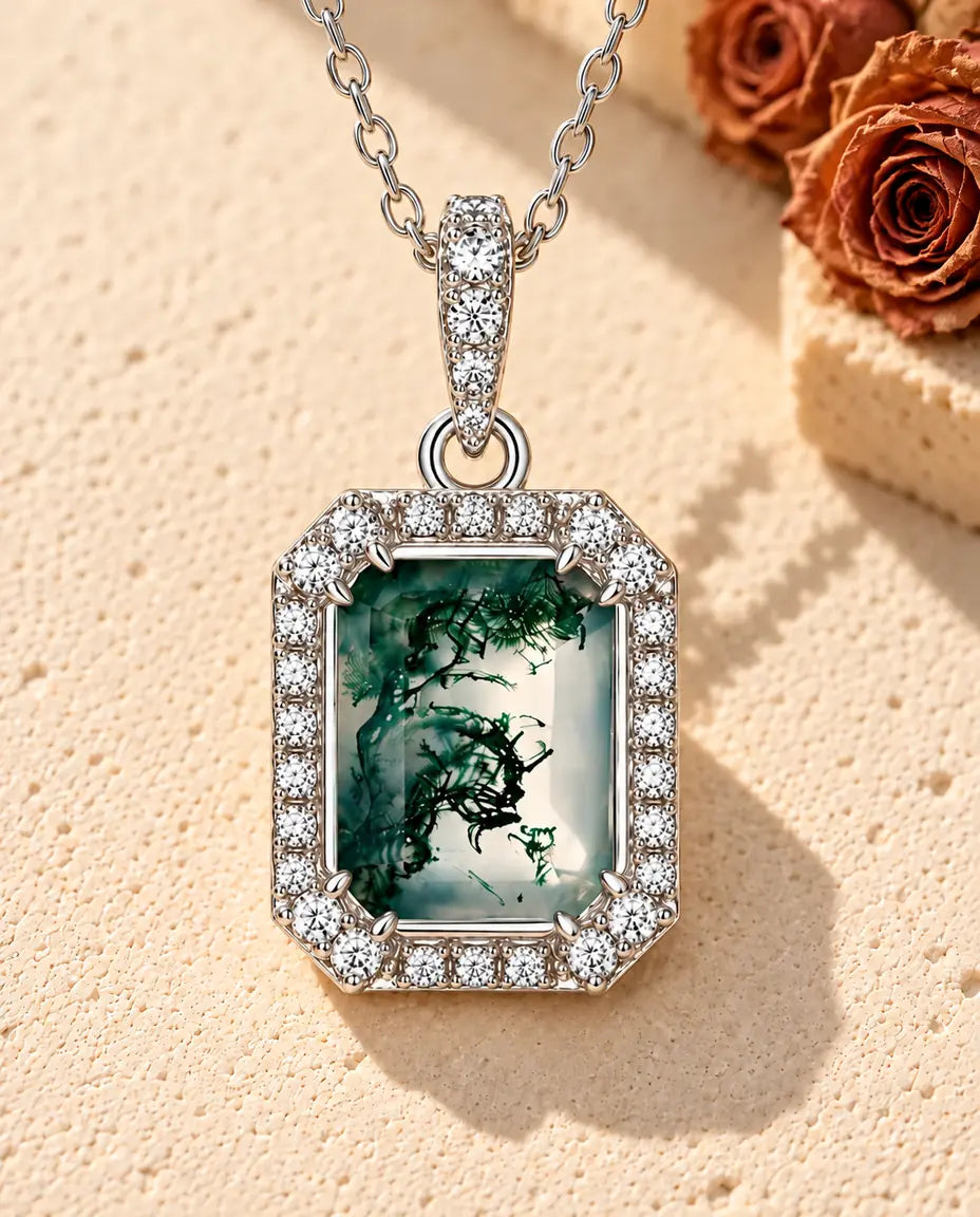 Halskæde i sølv med en grøn rektangulær moss agate i en ottekantet halo af små hvide zirkonia på beige puds foran travertin.