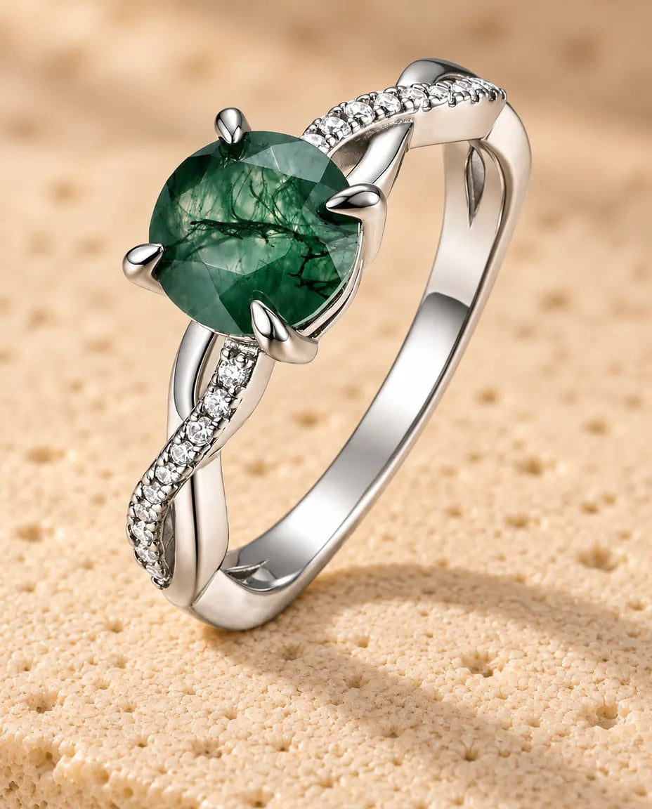 Sølvring med en rund, facetteret Moss Agate på en snoet ringskinne, stående på en plade af lys travertin i varmt sidelys.