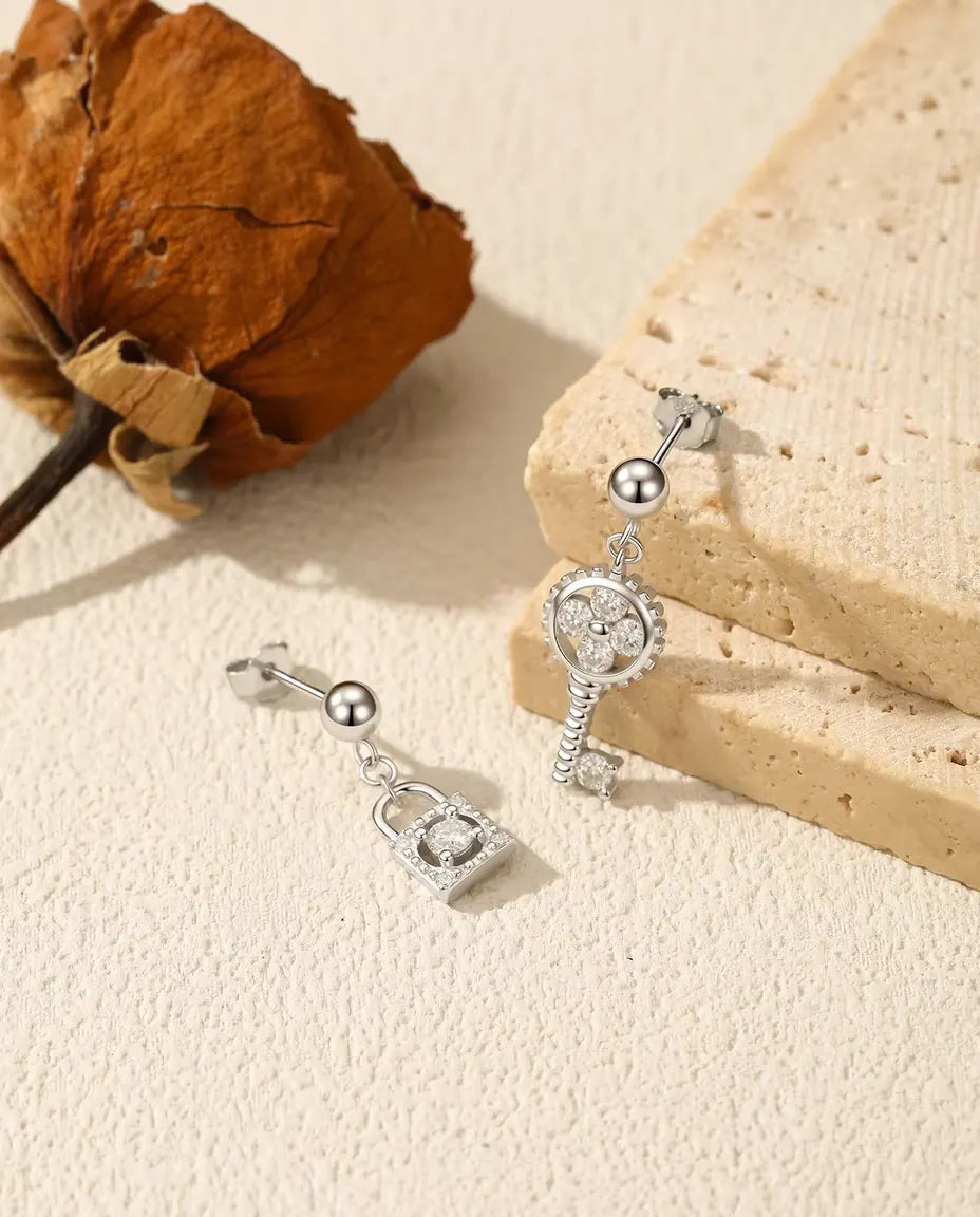 Asymmetriske sølvøreringe med en nøgle i det ene øre og en hængelås i det andet, sat med moissanite.