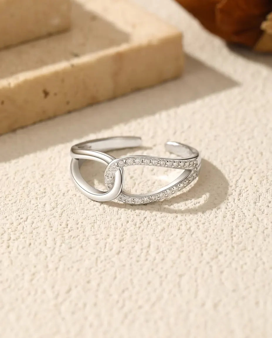 Bred sølvring med to sammenflettede ovale løkker, den ene med dobbelt række zirkoner, i 925 sterling sølv.