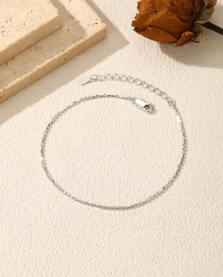 Meget tyndt diamantslebet armbånd i 925 sterling sølv ligger på groft puds med karabinlås, forlænger og en tørret blomst.