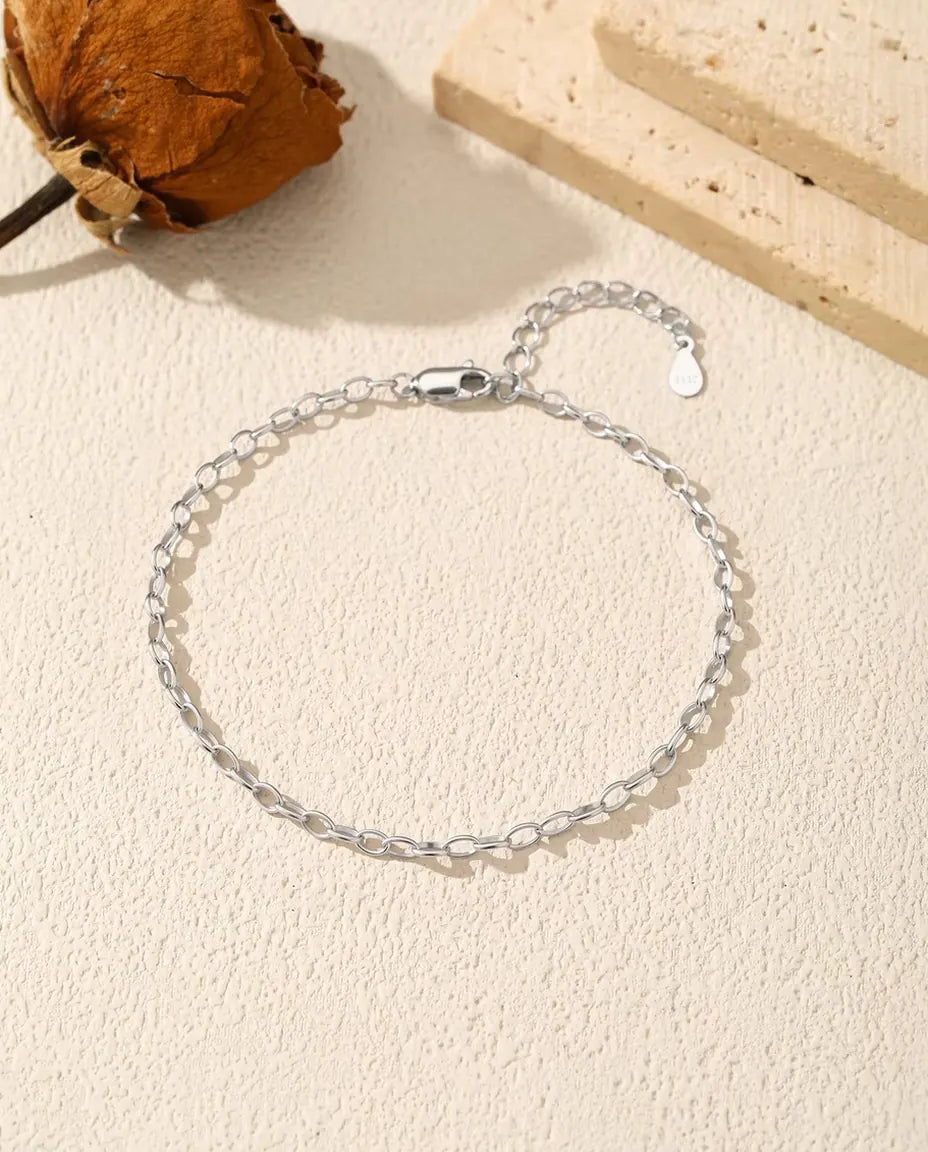 Armbånd med ovale led i 925 sterling sølv lagt i en cirkel på råhvid puds, med kort forlænger og lille sølvdråbe.