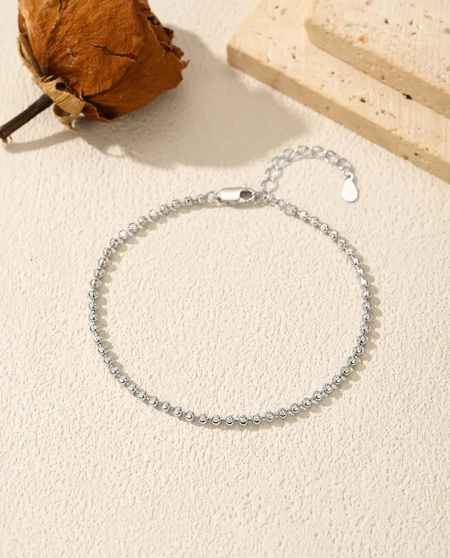 Armbånd af facetslebne perler i 925 sterling sølv ligger på groft puds med karabinlås, forlænger og en tørret blomst.