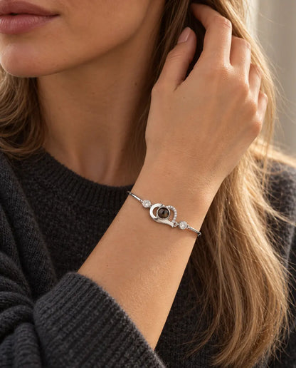 Kvinde med hånden i håret bærer det sølvfarvede armbånd med åbent hjerte og billede indeni