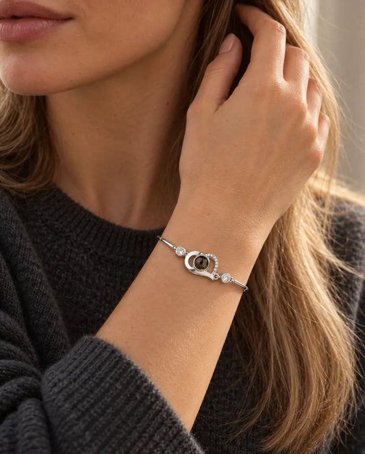 Kvinde med hånden i håret bærer det sølvfarvede armbånd med åbent hjerte og billede indeni