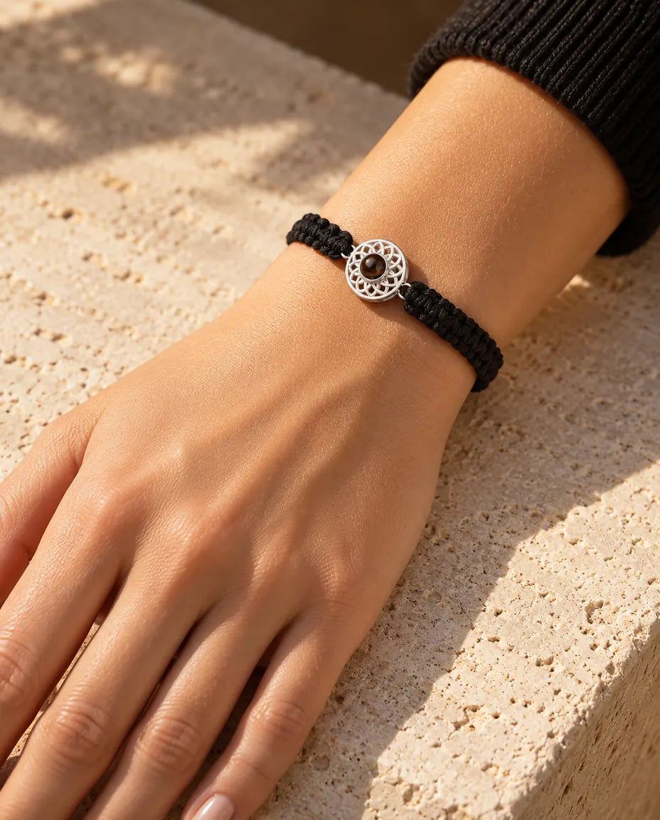 Kvinde med det sorte flettede armbånd og en sølvfarvet rund charm om håndleddet i varmt sollys
