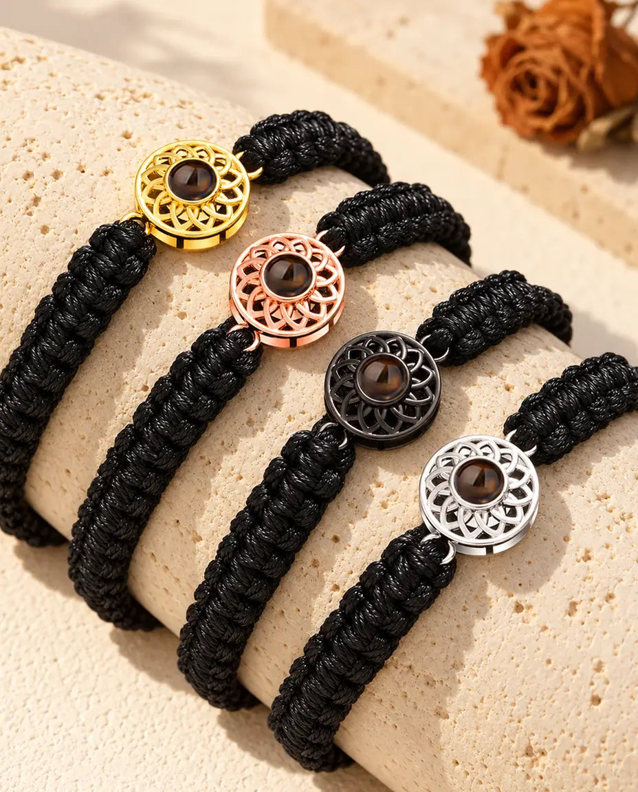 Fire sorte flettede armbånd med runde charms i alle farver, draperet over en blok travertin