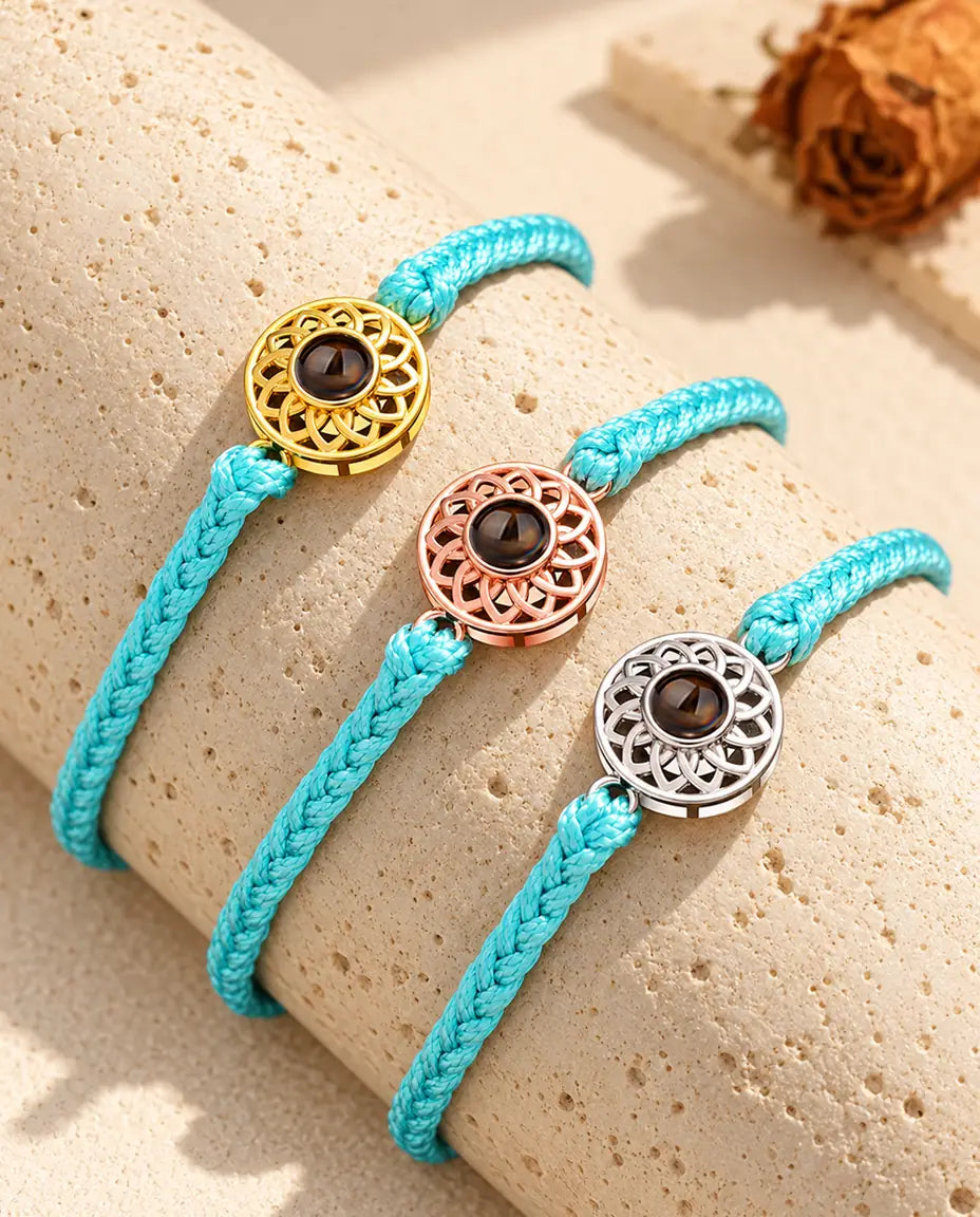 Tynde blå flettede armbånd med runde charms i guldfarvet, rosaguldfarvet og sølvfarvet på travertin