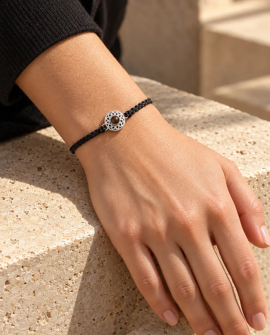 Kvinde med det tynde sorte flettede armbånd og en sølvfarvet rund charm om håndleddet i varmt sollys