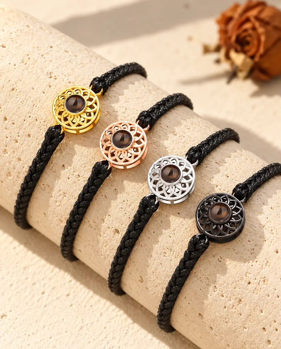 Fire tynde sorte flettede armbånd med runde charms i alle farver, draperet over en blok travertin
