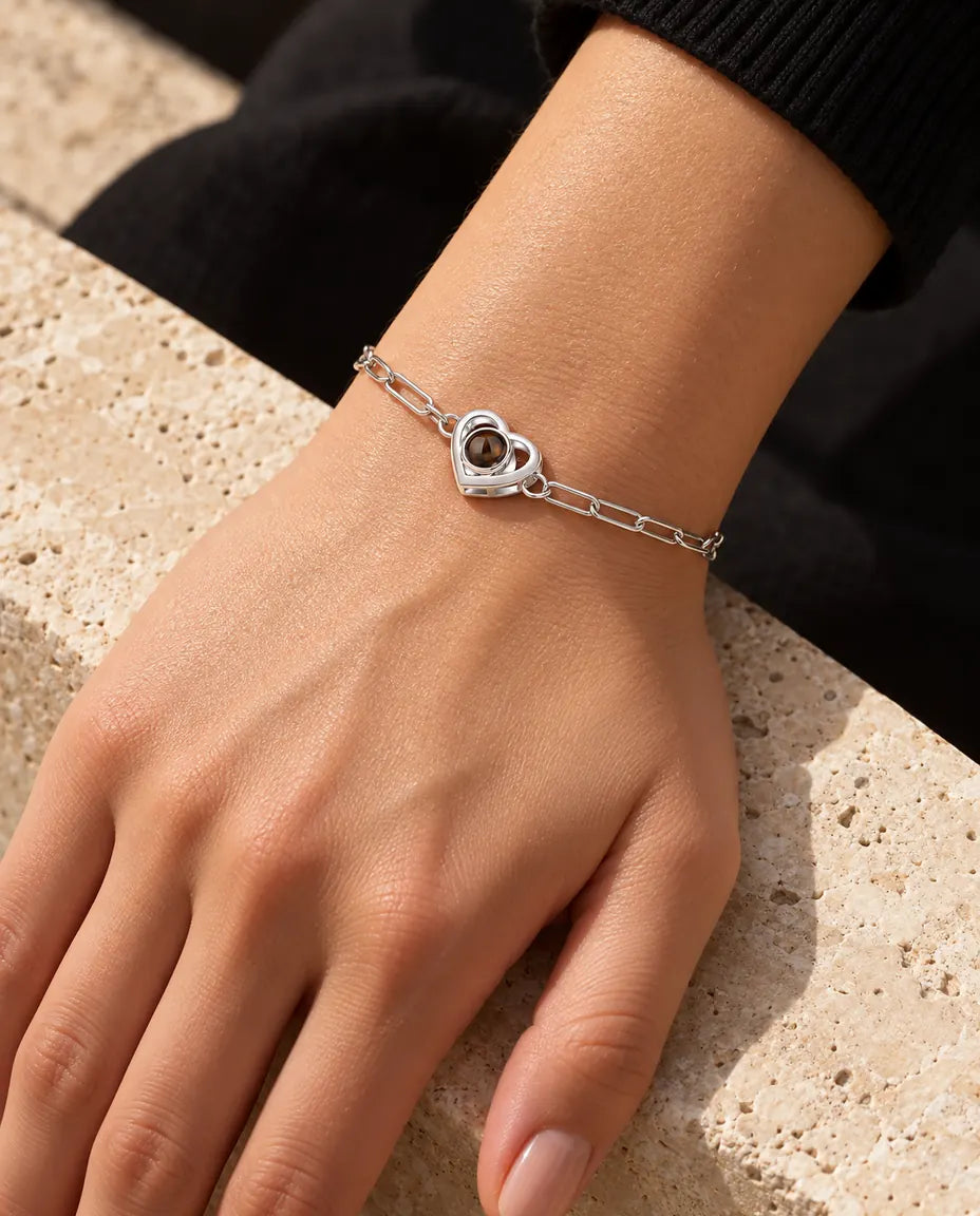 Kvinde med det sølvfarvede armbånd med dobbelt hjerte og billede indeni om håndleddet i varmt sollys