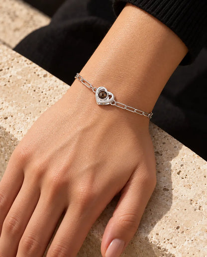 Kvinde med det sølvfarvede armbånd med dobbelt hjerte og billede indeni om håndleddet i varmt sollys