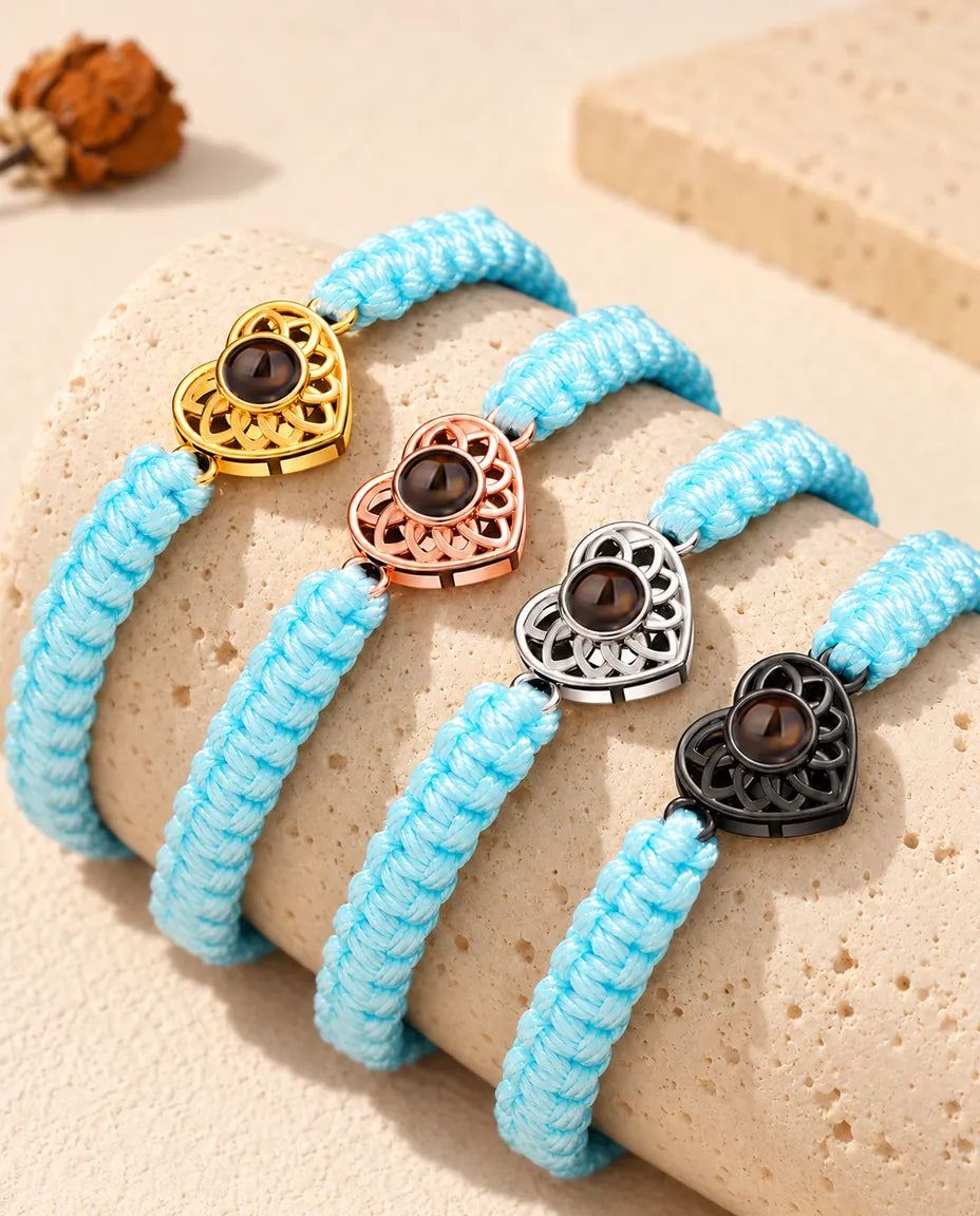 Lyseblå flettede armbånd med billede indeni stillet op på en travertinblok i hver charmfarve