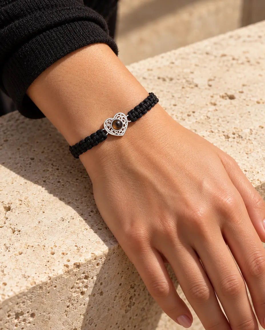 Kvinde med det sorte flettede armbånd og en sølvfarvet hjertecharm om håndleddet i varmt sollys