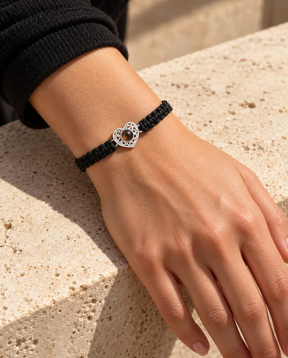 Kvinde med det sorte flettede armbånd og en sølvfarvet hjertecharm om håndleddet i varmt sollys