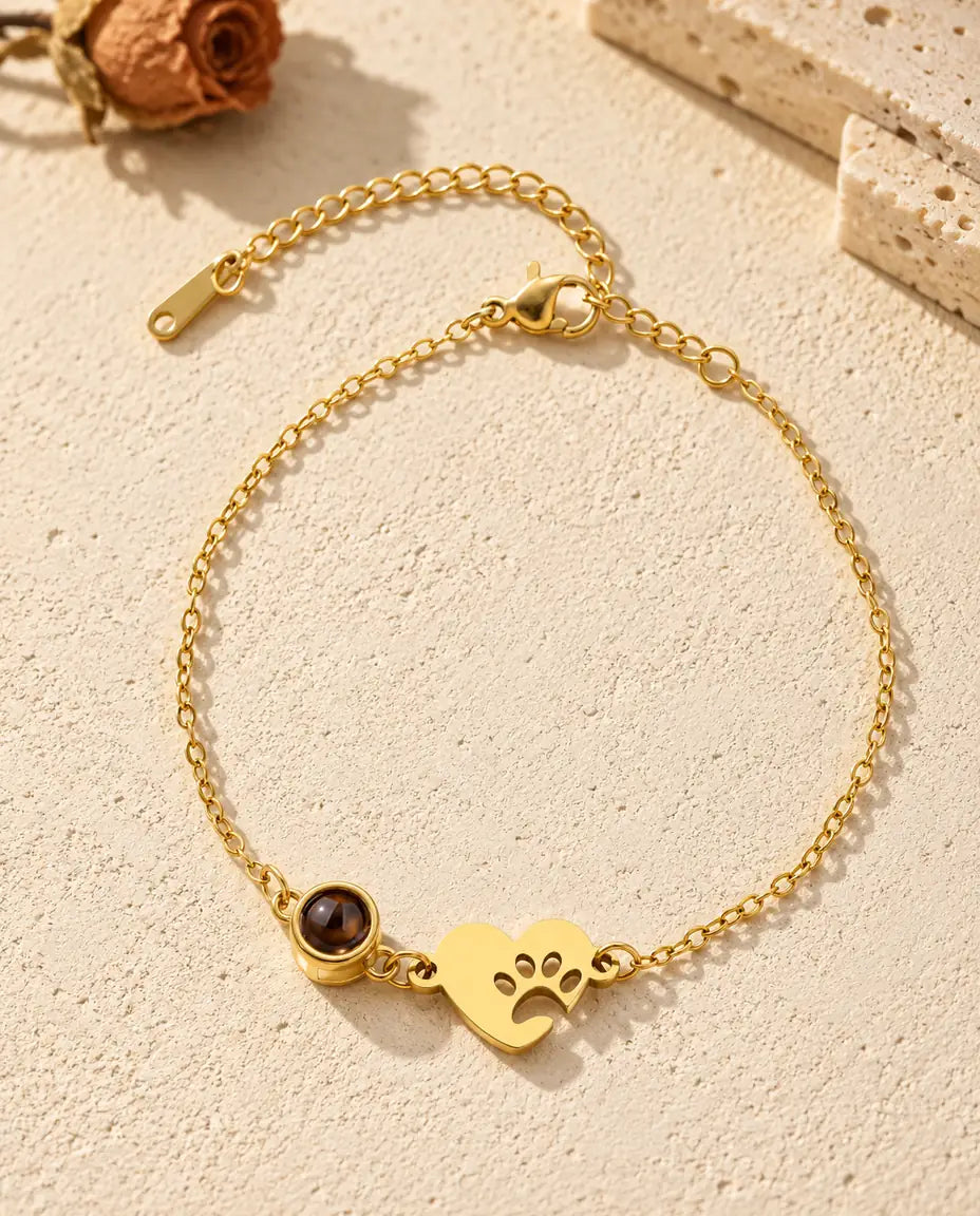Det guldfarvede armbånd med poteaftrykshjerte og billede indeni set ovenfra