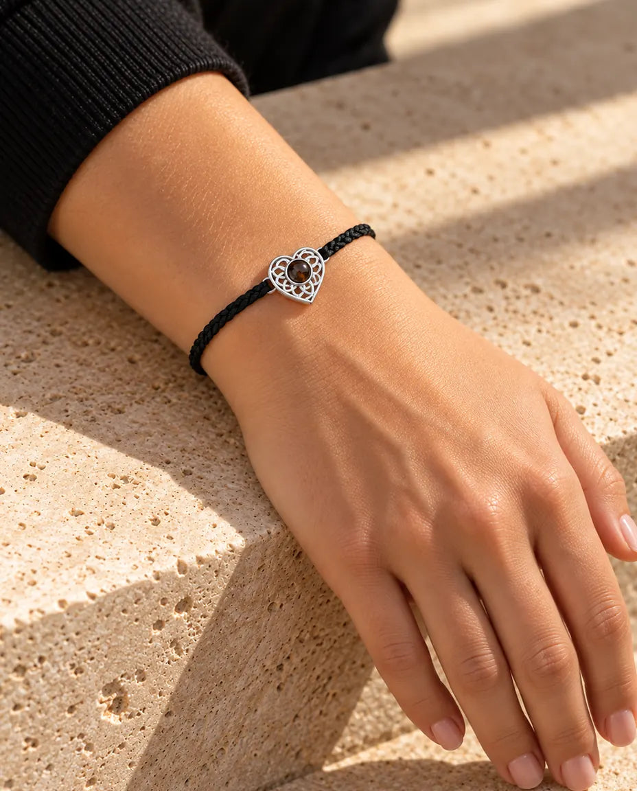 Kvinde med det tynde sorte flettede armbånd og en sølvfarvet hjertecharm om håndleddet i varmt sollys