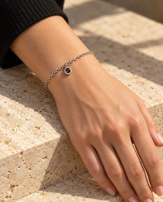 Kvinde med det sølvfarvede armbånd med lille rund zirkoniacharm om håndleddet i varmt sollys