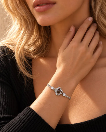 Kvinde rører ved siden af halsen og bærer det sølvfarvede armbånd med kærlighedsknude og billede indeni