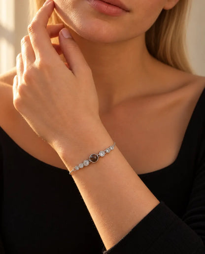 Kvinde rører ved sin kæbe og bærer det sølvfarvede armbånd med billede indeni og en række små sten