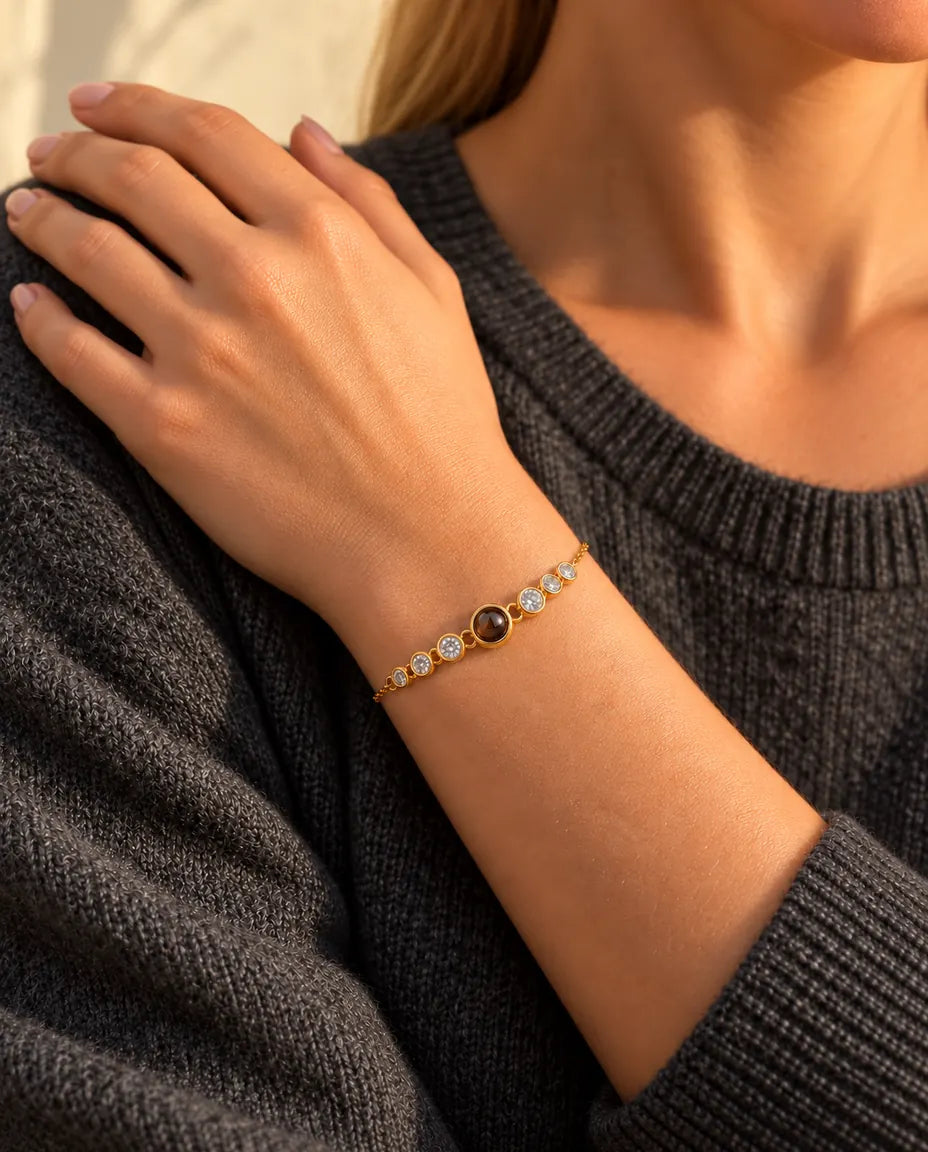 Nærbillede af det guldfarvede armbånd med zirkonia om håndleddet, hånden hviler på hendes skulder