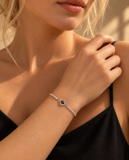 Kvinde med hånden på skulderen bærer det sølvfarvede tennisarmbånd med halo og billede indeni