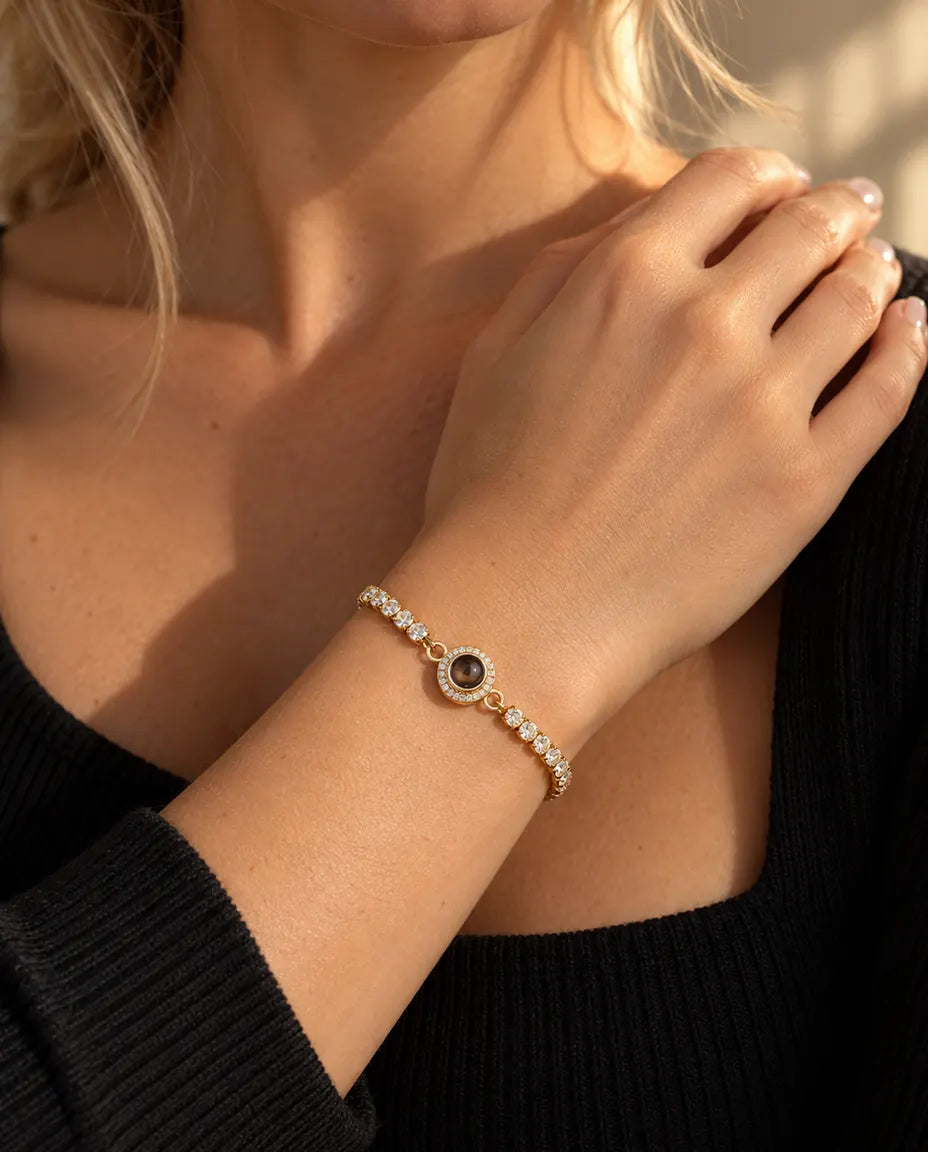 Nærbillede af det guldfarvede tennisarmbånd med halo-charm om et håndled ved kravebenet