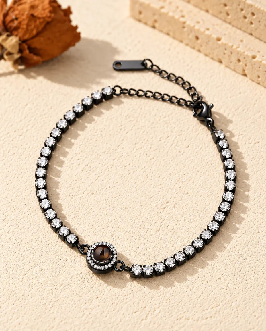 Sort tennisarmbånd med klare zirkonia og en halo-charm med projektionssten