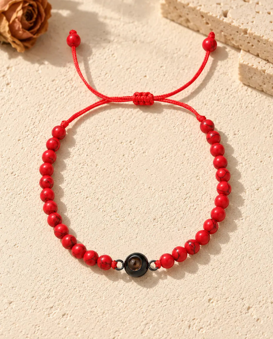 Armbånd med røde perler og en sort ringcharm set ovenfra med glideknude og snorender