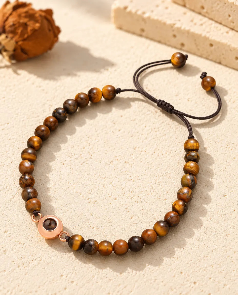 Armbånd med perler i tigerøje og en rosaguldfarvet ringcharm med billede indeni