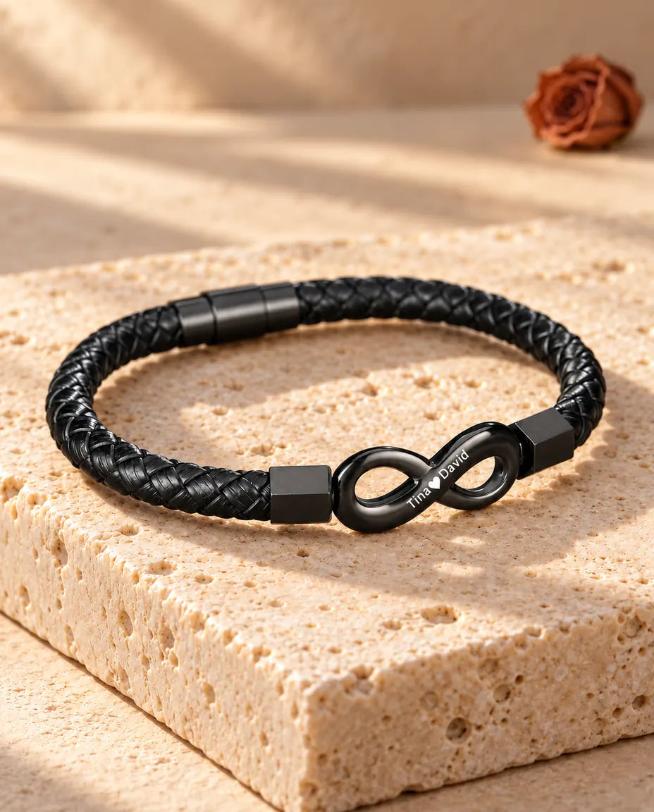 Armbånd til mænd med indgraveret uendelighedstegn og rund magnetlås, set fra en skrå vinkel på travertin