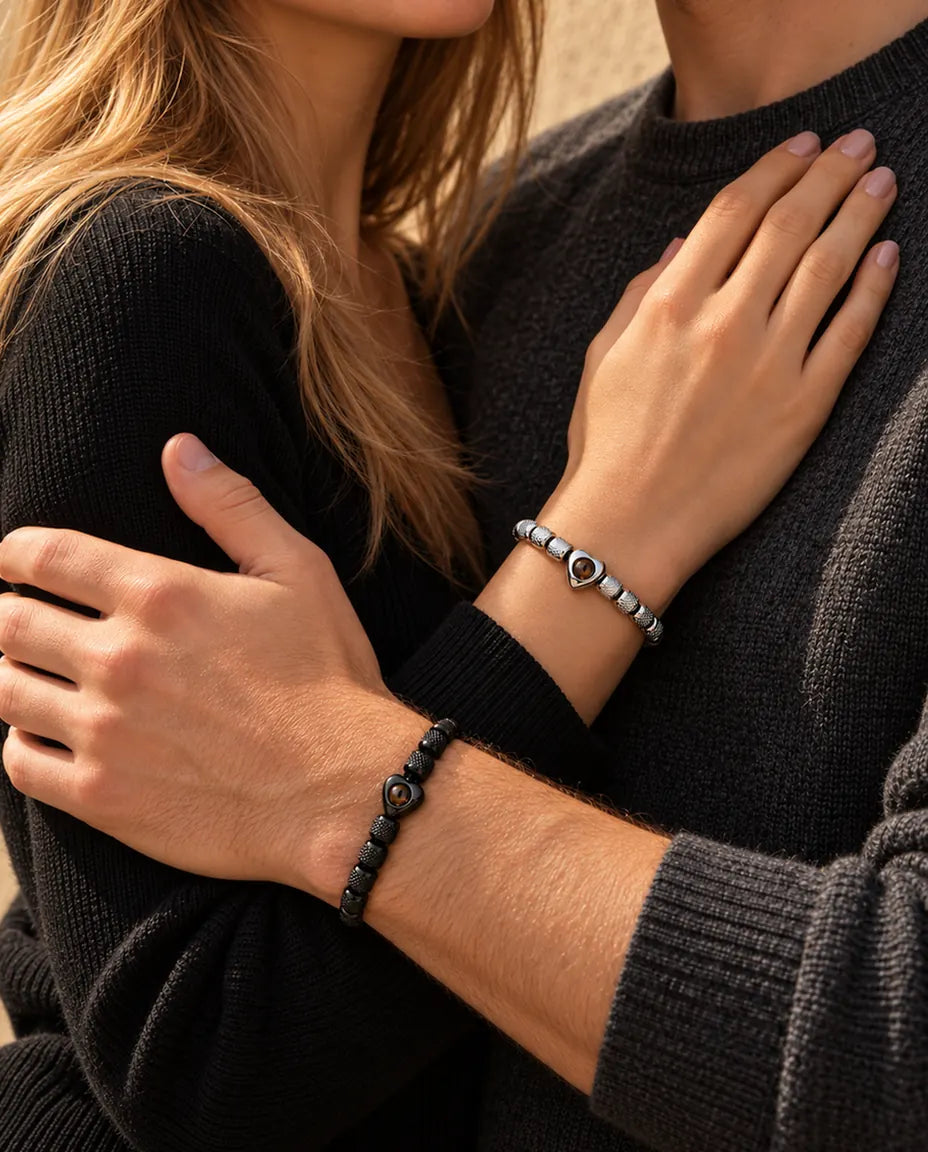 Par i en omfavnelse, hun bærer det sølvfarvede armbånd med hjerteperle og han det sorte
