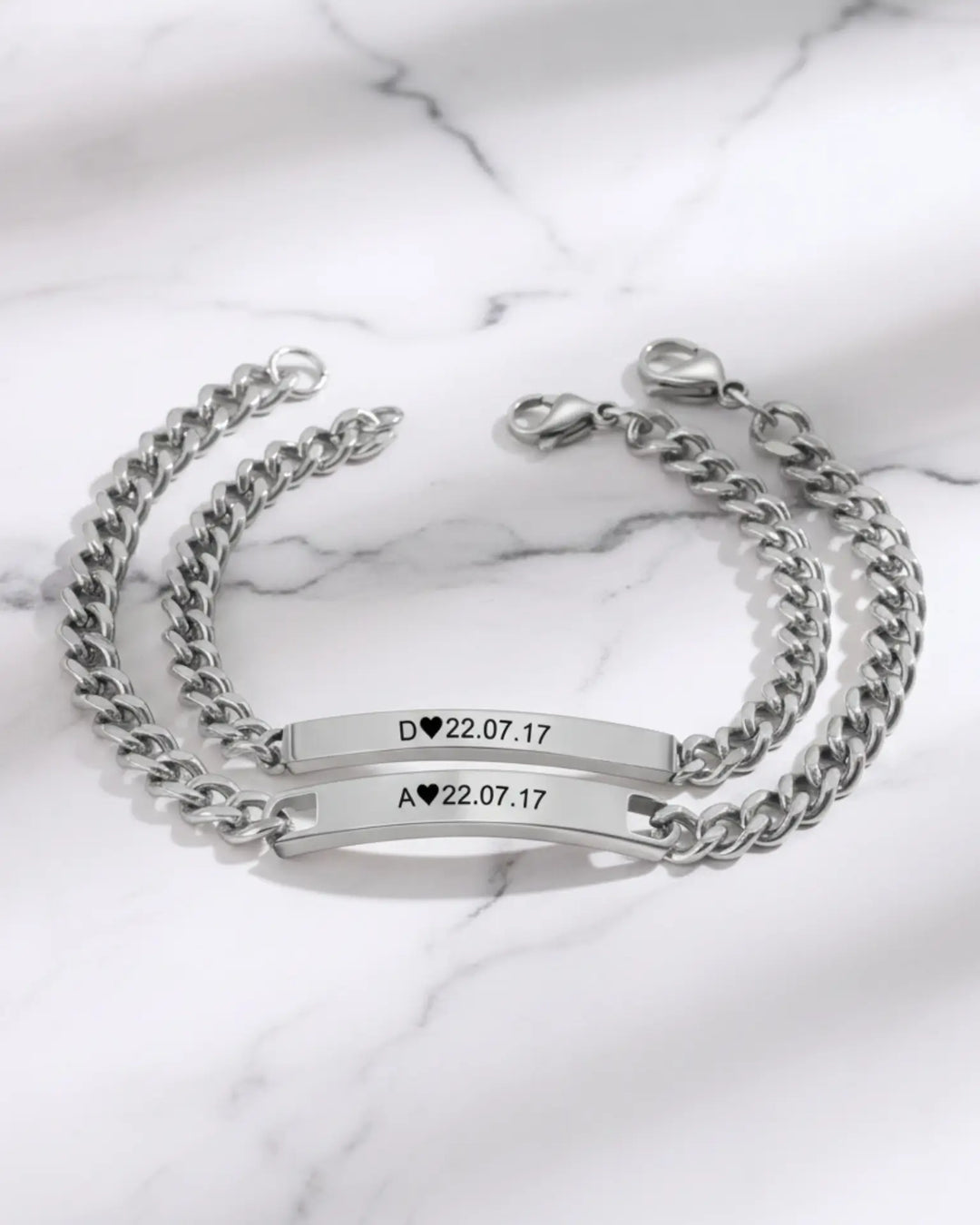 To matchende armbånd med kraftig panserkæde og en aflang plade med initialer og en dato indgraveret.