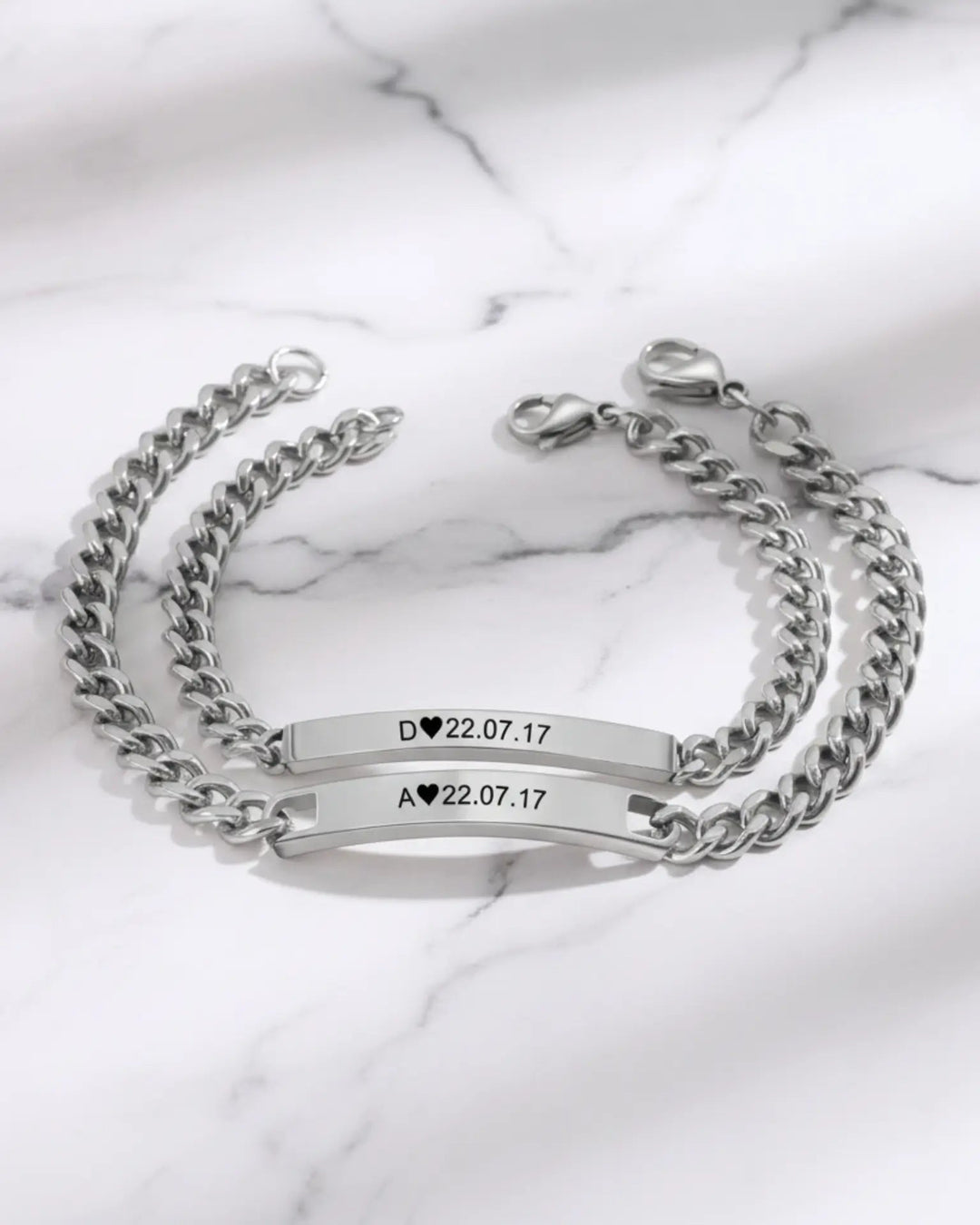 To matchende armbånd med kraftig panserkæde og en aflang plade med initialer og en dato indgraveret.