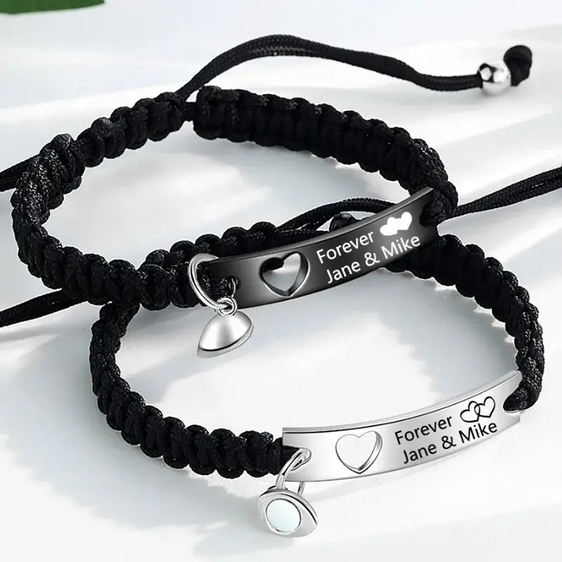 To armbånd i rustfrit stål, det ene sort og det andet sølvfarvet, med hver sin charm til indgravering.