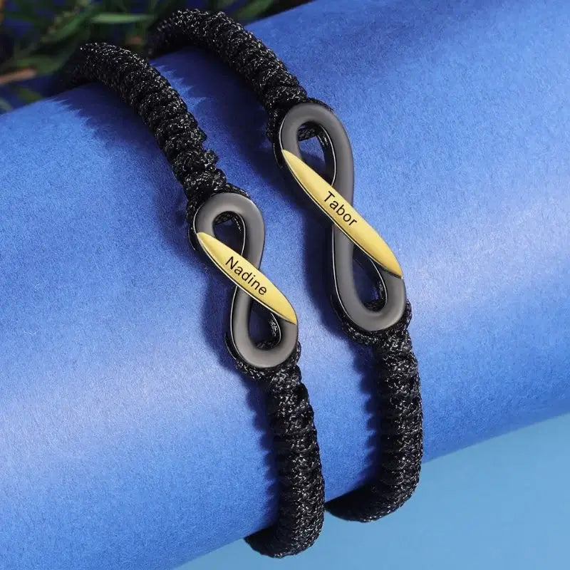 To sorte armbånd i kobber med uendelighedstegnet i midten og et navn indgraveret på hvert armbånd.
