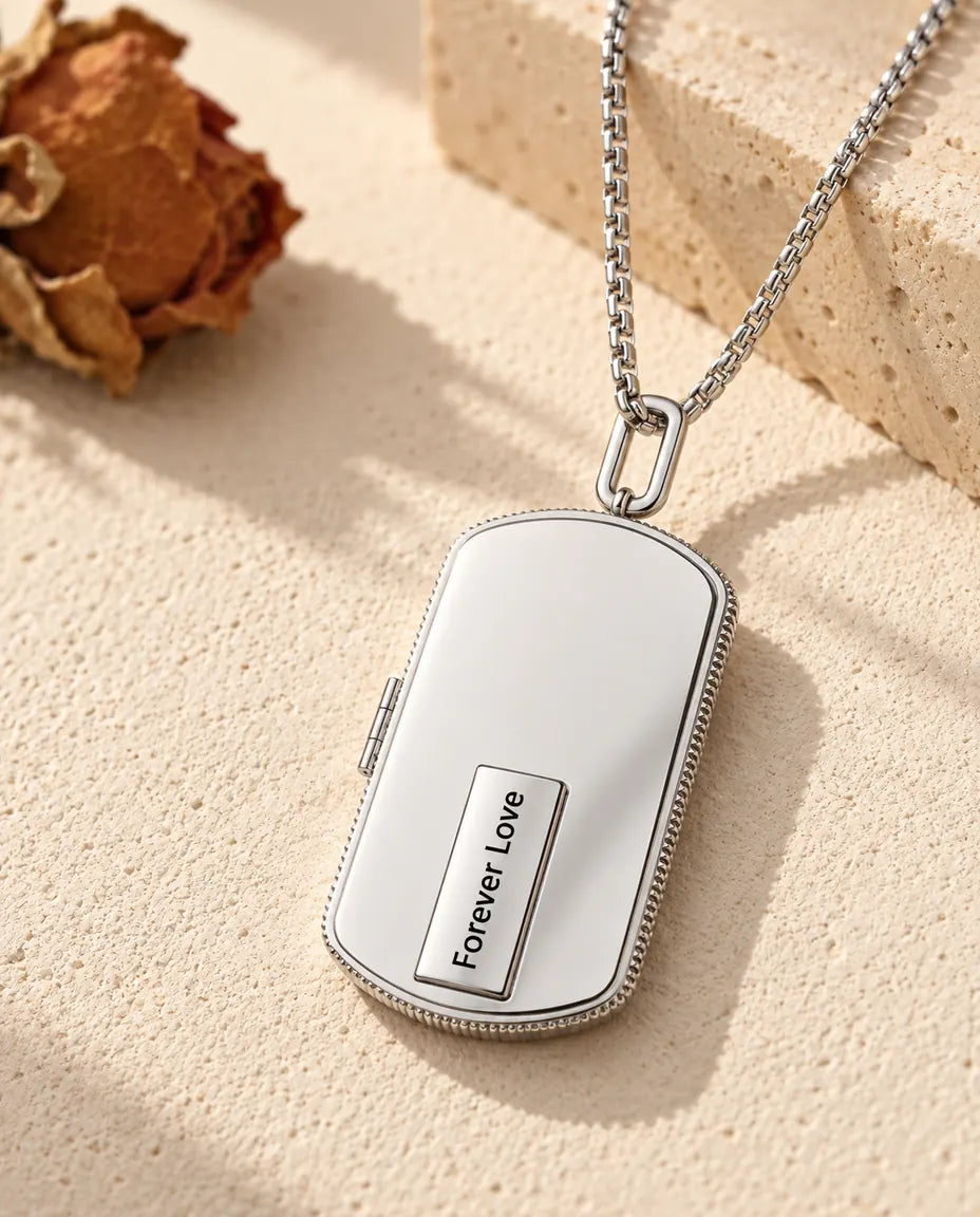 Sølvfarvet dog tag-medaljon i rustfrit stål med en lille plade indgraveret med Forever Love, liggende på en lys stenflade